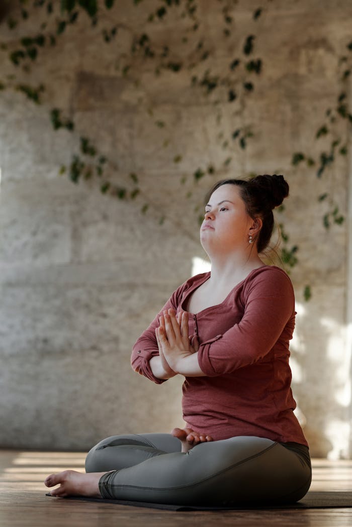 A young woman with Down syndrome focuses on inner peace while practicing yoga indoors.