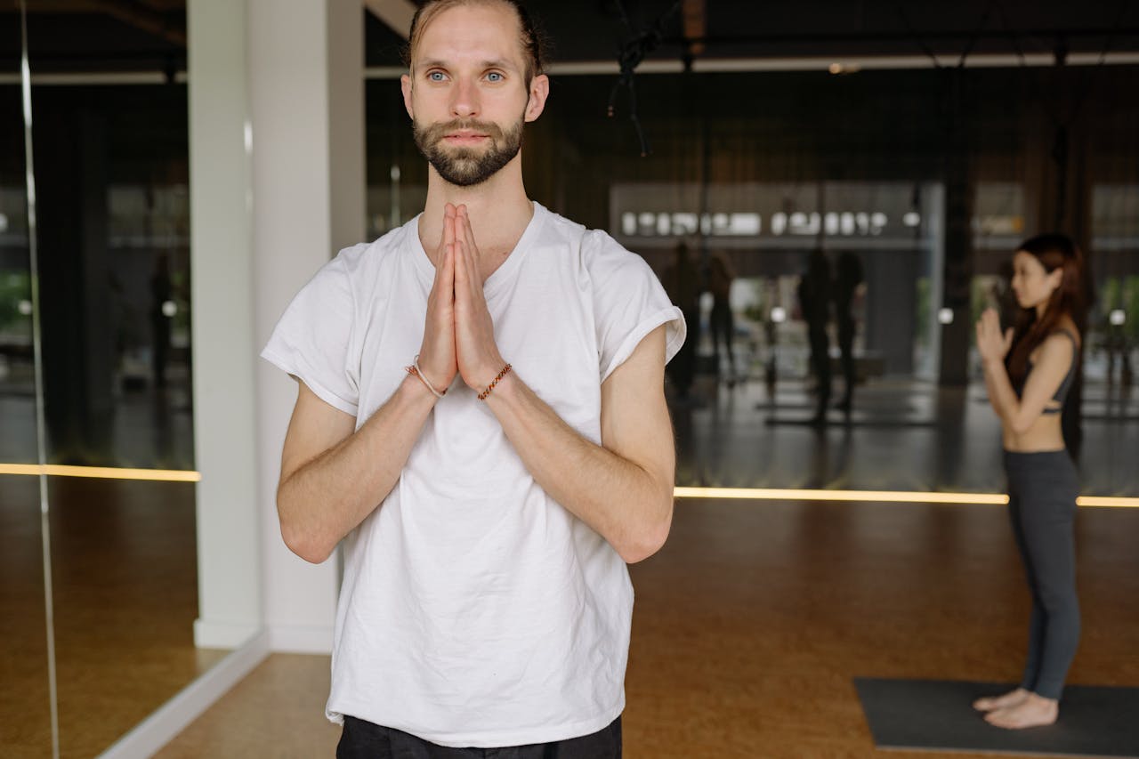 A man in a white shirt practicing yoga in a calm indoor studio, exemplifying mindfulness and relaxation.
